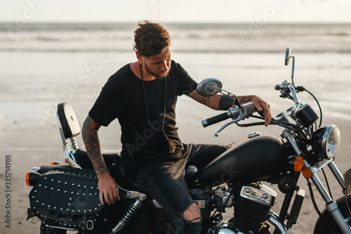 Biker man with his motorbike beside the oceanl, enjoying freedom and active lifestyle, having fun on a bikers tour sunset on the beach photo