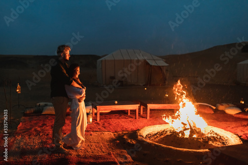 Couple hug in love near big campfire. Romantic night in glamping desert camp in Sahara, Morocco. Honeymoon. photo