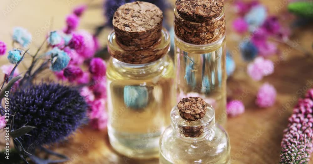 Aromatic perfume, scent, fragrance in glass bottles among fresh flowers. Purple, white, pink flowers with vials of essential oil closed cork caps on wooden background. Camera moves from down to up. Aromatic perfume, scent, fragrance in glass bottles among fresh flowers. Purple, white, pink flowers with vials of essential oil closed cork caps on wooden background. Camera moves from down to up.
