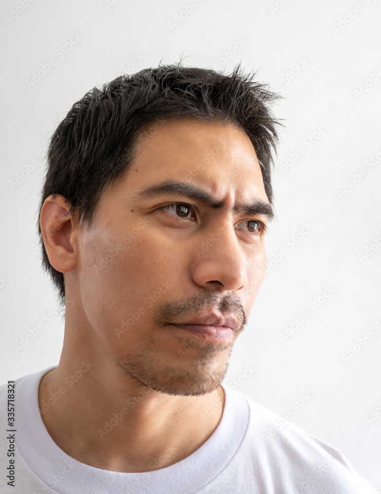 Fototapeta premium Portrait of a handsome Asian man in masculine look isolated on a white background. A serious and thoughtful adult man looks away from the camera. Close up, head shot face of the bearded male model.