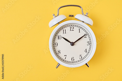 White retro alarm clock on the yellow background with copy space. Time concept