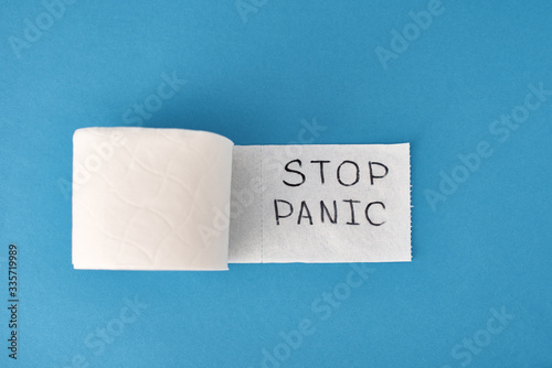 Panic buying Covid-19 Coronavirus outbreak concept. Roll of toilet paper with inscription stop panic and surgical mask on the blue background.
