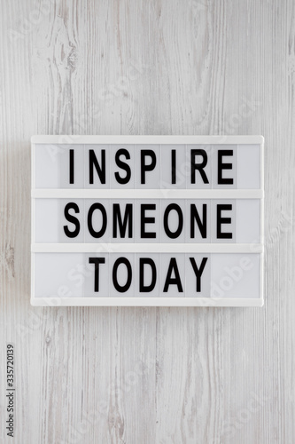 'Inspire someone today' words on a modern board on a white wooden background, top view. Overhead, from above, flat lay. Close-up.