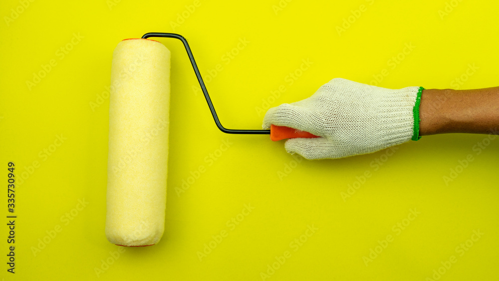 Obraz premium Hand holding painting wall with a paint roller on yellow wall.