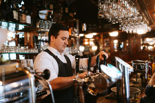 A young caucasian waiter pours beer at a bar