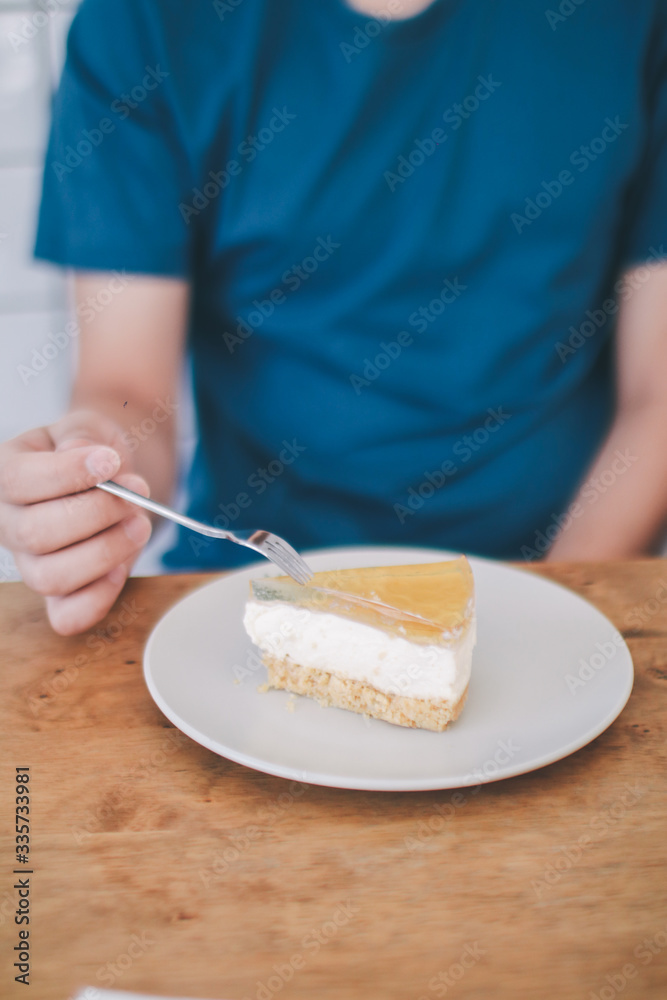 Man wear blue t-shirt sitting in coffee shop eating lemon cheesecake in white plate with folk.Tasty fresh homemade cream cheese sweet cake for breakfast.Eat delicious dessert is good for your mood. 