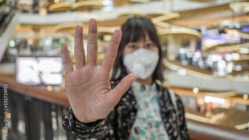 young woman in protective sterile medical mask on her face, show hand, stop no sign. Air pollution, virus. coronavirus concept.