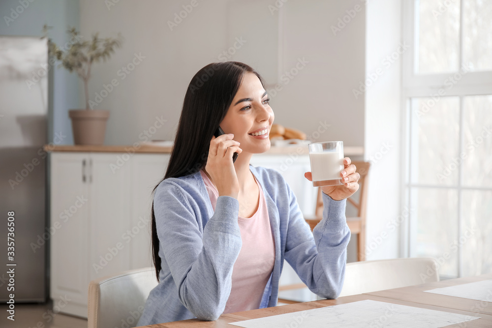 Beautiful young woman talking by phone while drinking milk in kitchen Beautiful young woman talking by phone while drinking milk in kitchen