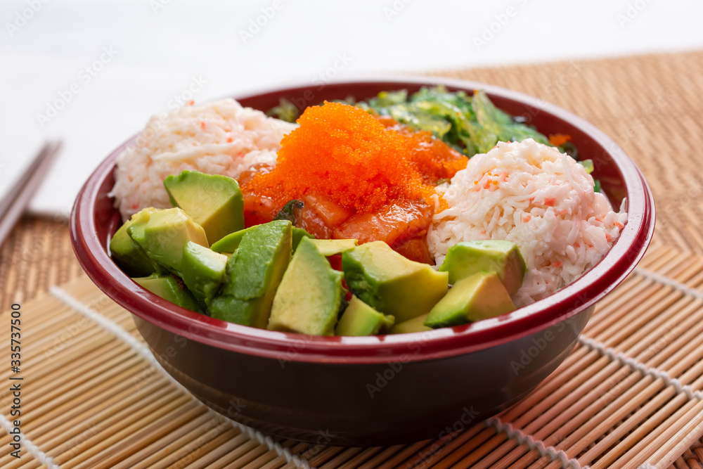 A view of a poke bowl with imitation crab meat, avocado and flying fish roe, in a restaurant or kitchen setting. A view of a poke bowl with imitation crab meat, avocado and flying fish roe, in a restaurant or kitchen setting.