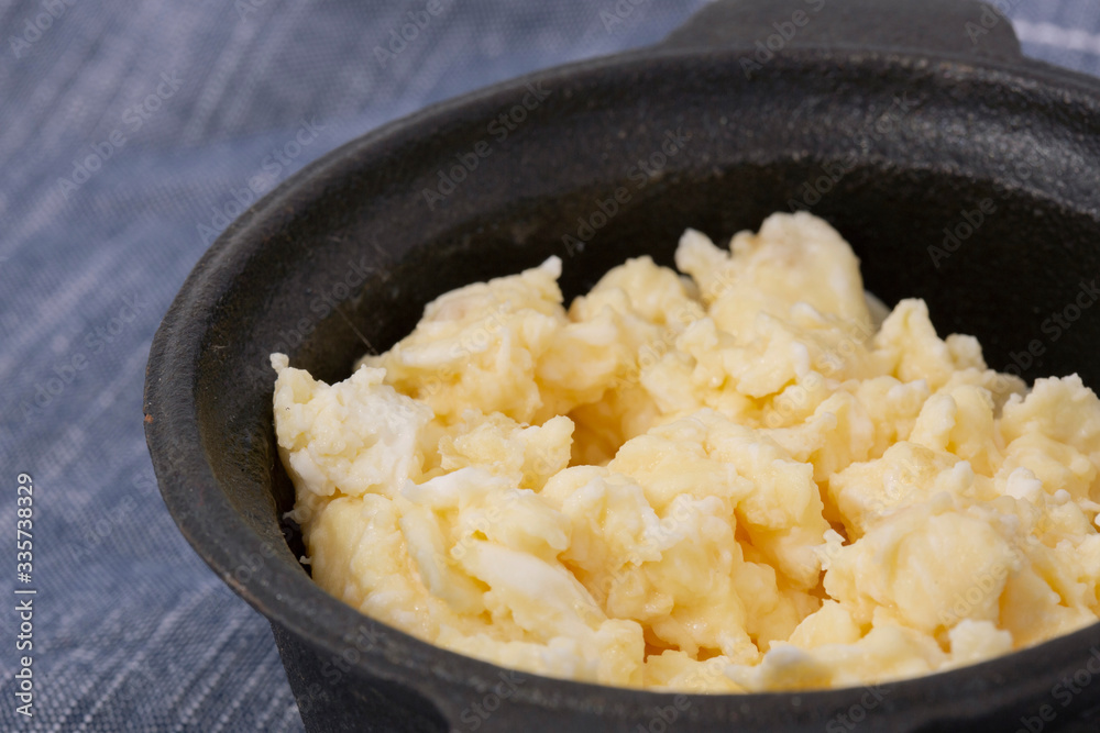 Scrambled egg in a traditional cast iron pot on a blue tea towel. On a patterned tile surface Scrambled egg in a traditional cast iron pot on a blue tea towel. On a patterned tile surface
