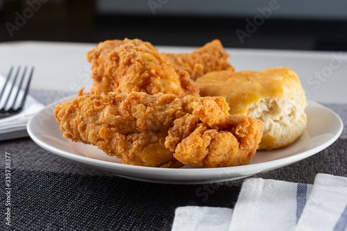 A view of a plate with fried chicken and biscuit, in a restaurant or kitchen setting.