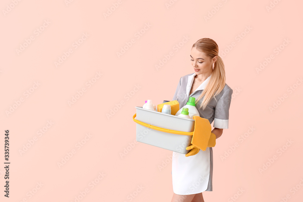 Beautiful young chambermaid with cleaning supplies on color background Beautiful young chambermaid with cleaning supplies on color background