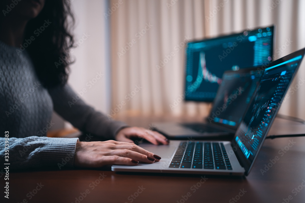 young female trader with laptop and screen looking at stock charts young female trader with laptop and screen looking at stock charts