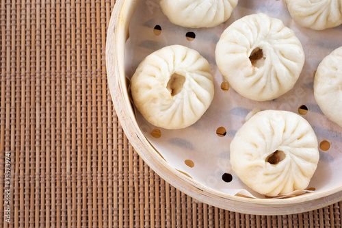 A top down view of a bamboo steamer of Chinese baozi, in a restaurant or kitchen setting.