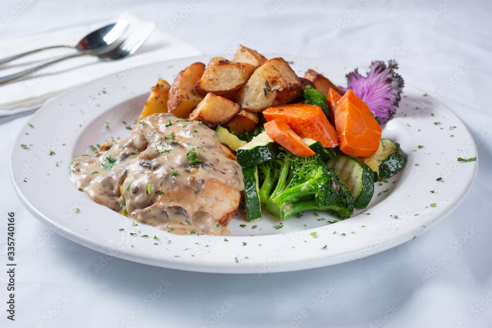 A view of a plate of chicken Florentine, with steamed veggies and roasted potatoes, in a restaurant or kitchen setting. A view of a plate of chicken Florentine, with steamed veggies and roasted potatoes, in a restaurant or kitchen setting.
