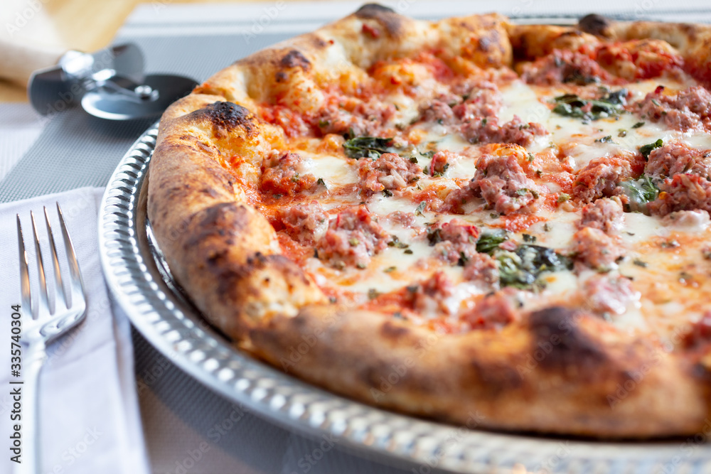 A closeup view of a rustic pizza pie in a restaurant or kitchen setting, featuring toppings such as sausage and herbs. A closeup view of a rustic pizza pie in a restaurant or kitchen setting, featuring toppings such as sausage and herbs.