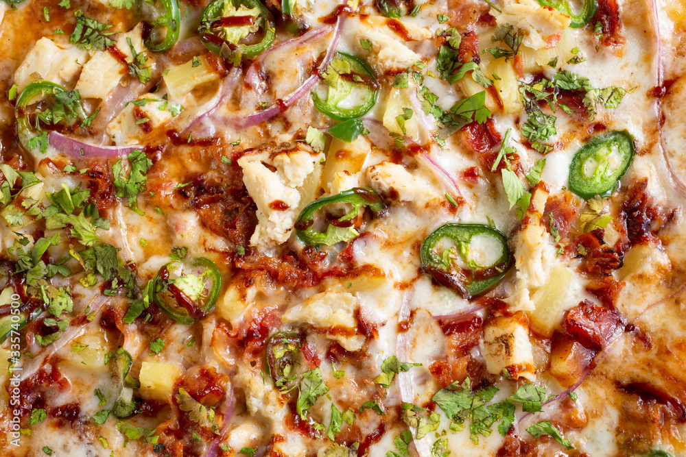 A top down view of a barbecue chicken and jalapeño pizza, in a restaurant or kitchen setting.