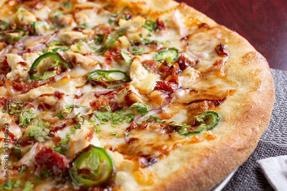 A closeup view of a barbecue chicken and jalapeño pizza, in a restaurant or kitchen setting.