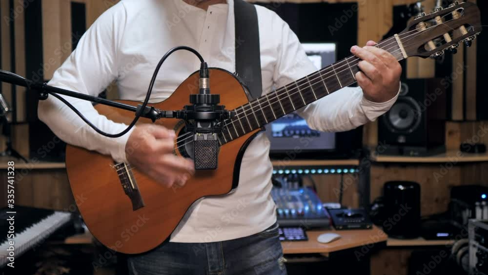 Static medium shot of a guitarist playing and recording a nylon string