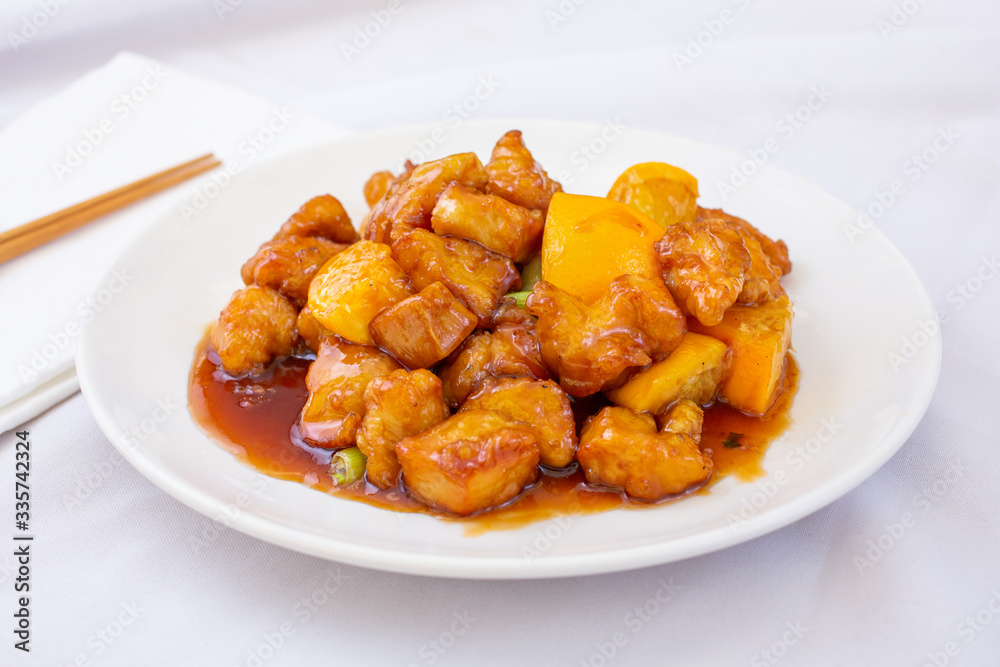 A view of a plate of Chinese orange chicken, in a restaurant or kitchen setting.