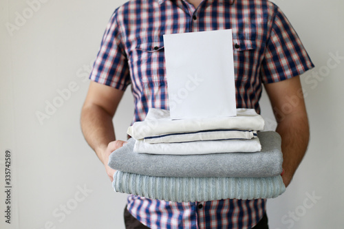 Housework and cleaning. Laundry day. Male hands with stack of washed clothes and laundry detergent box. Household concept