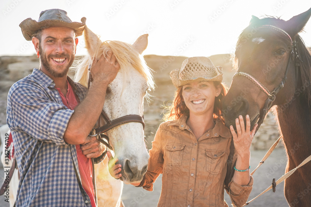 Animals lovers couple taking with bitless horses during sunny day inside ranch corral - Happy people having fun training at their farm - Love and wild concept - Focus on guys faces - obrazy, fototapety, plakaty 