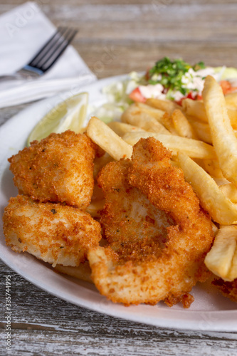 A closeup view of a deep fried shrimp plate, with a side of french fries, in a restaurant or kitchen setting.