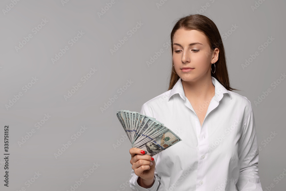 young businesswoman in white shirt holding dollar banknotes isolated on grey background young businesswoman in white shirt holding dollar banknotes isolated on grey background
