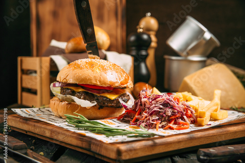 Appetizing cheeseburger with a knife and cole slow salad on the wooden board on the wooden background, side view, horizontal photo