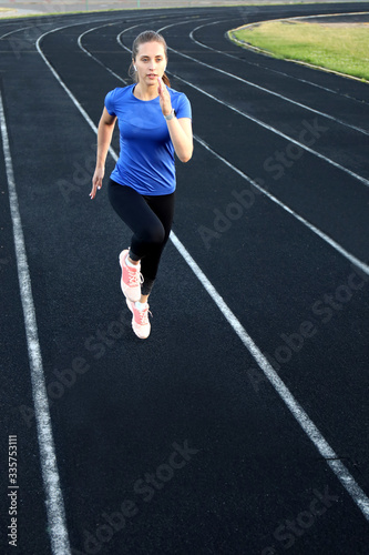 Runner athlete running on athletic track training her cardio in stadium. Jogging at fast pace for competition © ty