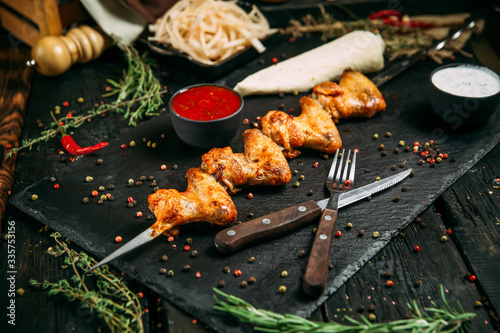 appetizing chicken wings kebab stick with red sauce and pickled onion on a black board on a dark wooden background, side view, horizontal