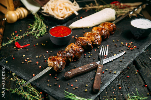 appetizing liver kebab stick with red sauce and pickled onion on a black board on a dark wooden background, side view, horizontal