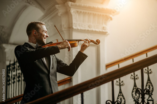 talented professional caucasian male violinist play in the hall, practice before performance. classical music concept. man in suit perform music using violin photo