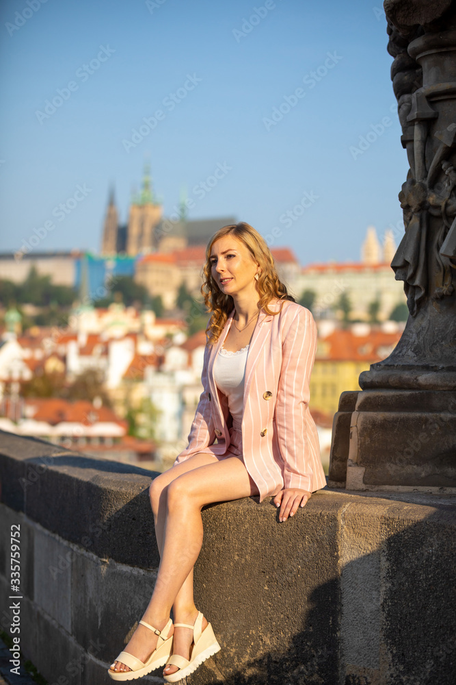 Young blonde woman walks along Charles Bridge in Prague in sunny day