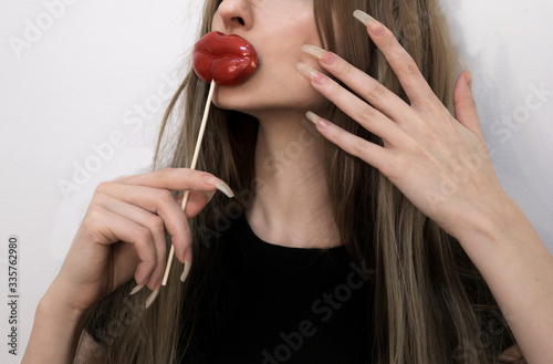 Cropped portrait of girl with long natural nails holds red lips shaped candy near the mouth