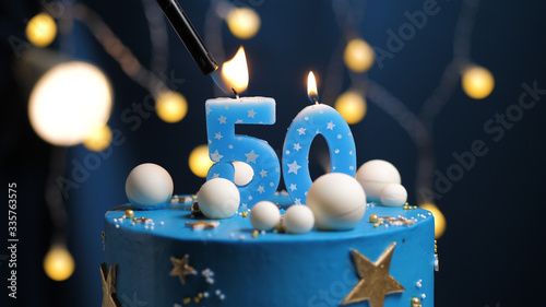 Birthday cake number 50 stars sky and moon concept, blue candle is fire by lighter. Copy space on right side of screen. Close-up