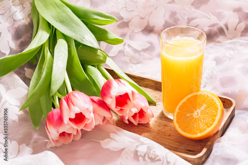 Healthy orange juice in bed on a wooden tray and white-pink bouquet of fresh cut tulips. Horizontal view