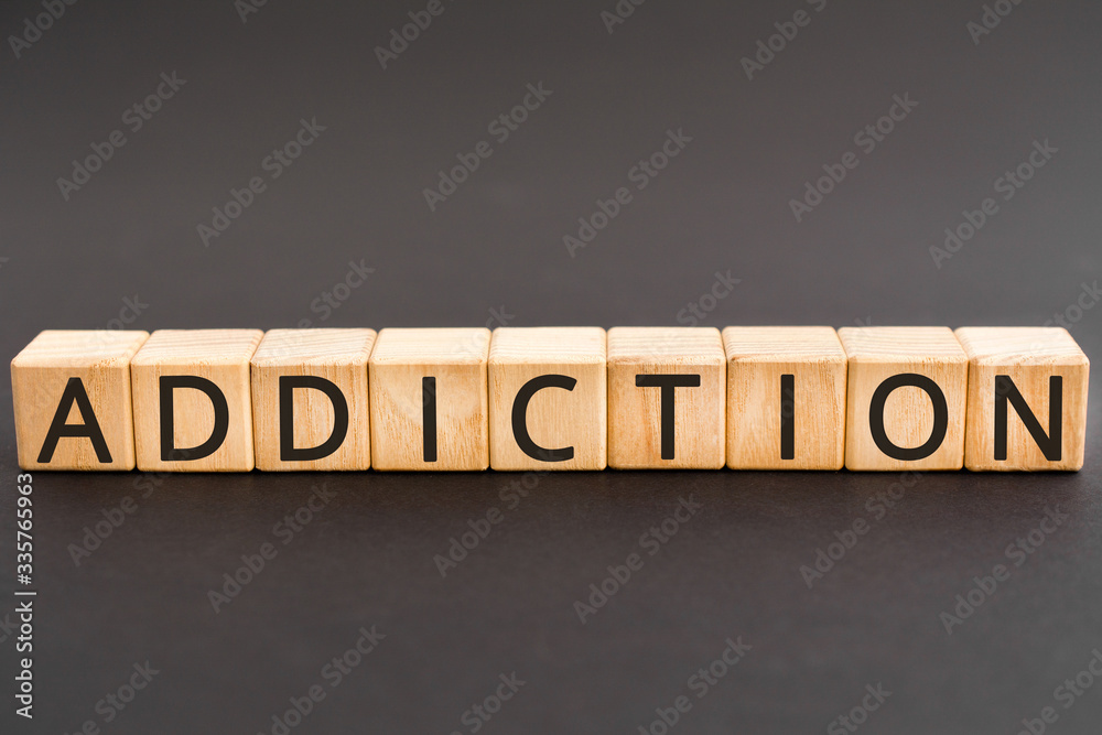 Naklejka premium Addiction - word from wooden blocks with letters, an inability to stop doing or using something addiction concept, black background