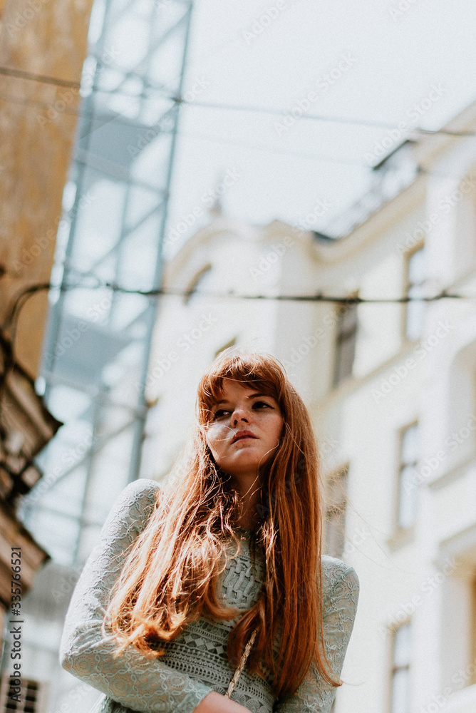 Fototapeta premium Stylish urban young redhair woman in a fashionable green dress posing in the street. European modern cute model girl enjoys a walk in the city. Spring fashion.