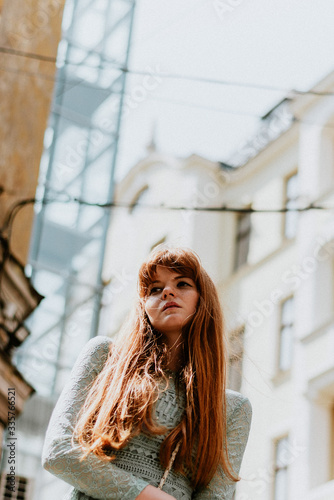 Stylish urban young redhair woman in a fashionable green dress posing in the street. European modern cute model girl enjoys a walk in the city. Spring fashion.