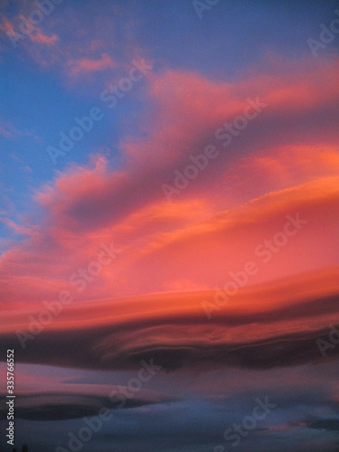 Pnk orange lenticular clouds form in the sky at sunset