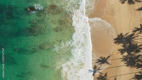 Haena. Aerial top down view over clear, transparent ocean water boiling and foaming at the shore, washing the golden sand of the beach. Bright sun enlightens the gorgeous tropical nature of Hawaii. 4K photo