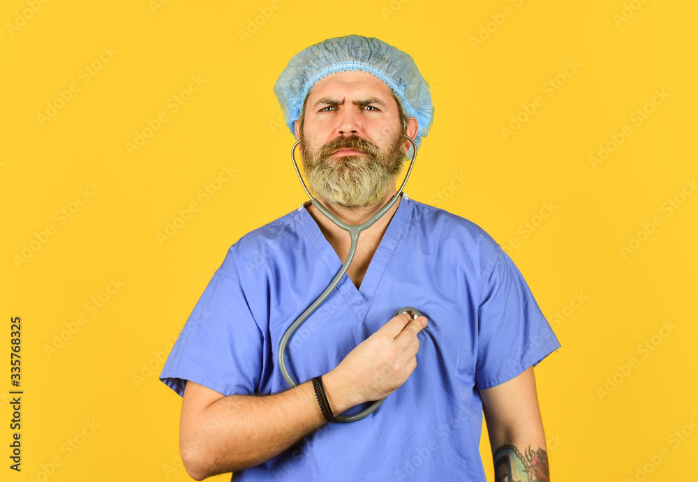 Doctor in blue medical coat. Polyclinic and hospital. bearded doctor use phonendoscope. listening his heart beating. Pathogen leads to pneumonia. heart attack. virus infection from china Doctor in blue medical coat. Polyclinic and hospital. bearded doctor use phonendoscope. listening his heart beating. Pathogen leads to pneumonia. heart attack. virus infection from china