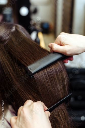 Close-up of a hairdresser straightening long brown hair with hair irons