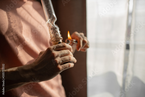 cropped photo of young man heating bong with a lighter. legalization of marijuana, cannabis, hemp concept. man smoke at home. unhealthy lifestyle, drugs concept
