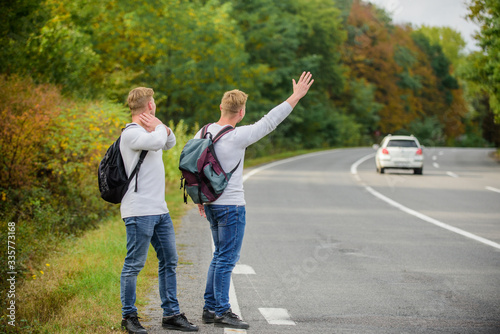 Try to stop some car. Reason people pick up hitchhikers. Missed their bus. Need help. Cheap transport. Transport problem. Travel and transport concept. Twins men at edge of road nature background