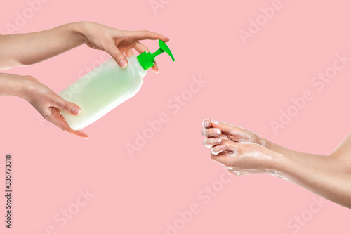 Concept of disinfection and protection from viruses.Women s hands are washed with soap at the bottom  and women s hands with antibacterial liquid soap at the top. Hands close-up.Pink background