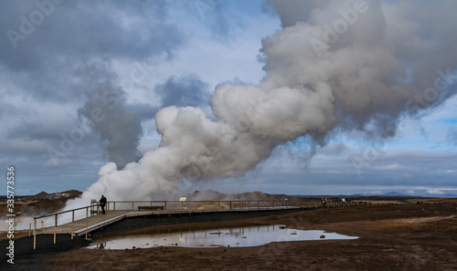 Geothermal area in Iceland. Lonely person. Powerful steam jet above the ground. A smoking geyser on a background of yellow clay and a cloudy sky. Reykjanes Peninsula