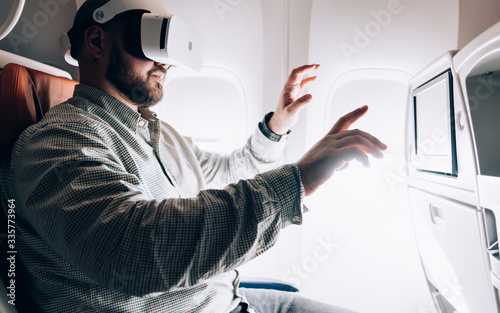 Man in VR glasses projecting 3d dimension during aircraft flight in business class with wifi connection, millennial male passenger testing imaginary environment while watching 3d video cinema