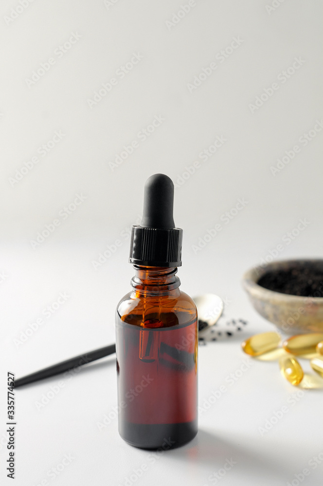 Glass bottle and pills of black cumin seeds essential oil. Nigella Sativa in spoon and bowl on white background